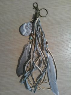 an assortment of feathers hanging from a hook on a wooden table with beads and leather cord