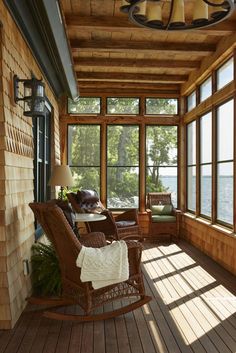 a porch with rocking chairs and windows overlooking the water is shown in this photo from inside