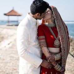 a man and woman in wedding attire kissing each other on the beach near the ocean