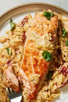 a white plate topped with pasta and meat next to a fork on top of a table