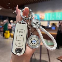 a hand holding a white key chain with two keys attached to it and a remote control on the other side