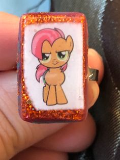 someone is holding a little pony ring with glitters on it's sides and has an image of pinkie ponies in the middle