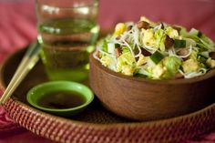 a wooden bowl filled with salad and chopsticks next to a green cup on a table