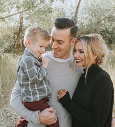 a man, woman and child are smiling for the camera while standing in front of some trees