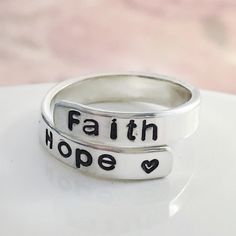 Does the phrase ''faith hope love'' bring peace and meaning to your heart? Faith, hope, ''love'' or cross is hand stamped on wrap ring in your choice of metal. I personally love to wear this ring on my middle finger, thumb, and pinky. It is adjustable so you may be able to squeeze it or stretch it a little for various fingers. These make great gifts since they are adjustable. QUANTITY This listing is for one item unless you choose more. FEATURES 4mm wide .925 sterling silver, 14K rose gold fille Inspirational Adjustable Ring, Inspirational Silver Promise Ring, Personalized Inspirational Ring Jewelry, Inspirational Personalized Ring Jewelry, Inspirational Hand Stamped Promise Ring, Christian Jewelry For Women, Ring Wrap, Name Rings, Wrap Ring