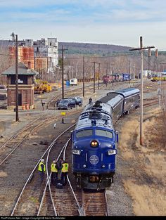 a blue train traveling down train tracks next to a loading area with cars on it