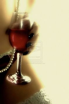 a woman holding a wine glass with red liquid in it's hand while wearing pearls