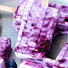 three popsicles with blueberries and ice cream on them, sitting next to some berries