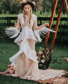 a woman with long hair wearing a white dress standing in front of a wooden ladder