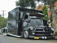 a black semi truck parked on the side of the road next to a tree and building