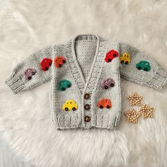 a knitted sweater with cars on it next to some buttons and beads laying on a white furnishing