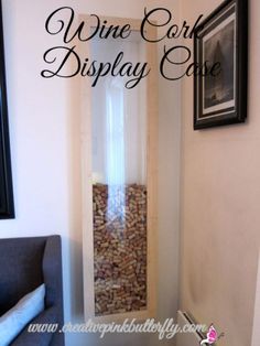 a wine cellar display case in the corner of a room with a couch and pictures on the wall