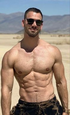 a shirtless man with no shirt standing in the desert wearing sunglasses and looking at the camera