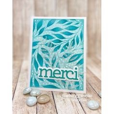 a card with leaves and the word merci written in white on it, surrounded by pebbles