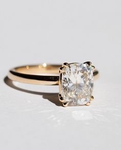 an engagement ring with a cushion cut diamond in the center, on a white surface