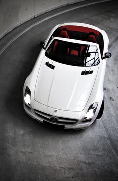 a white sports car driving on a curved road with its hood up and the top down