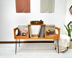 a wooden table topped with books next to a white chair and potted plant on top of a hard wood floor