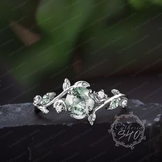 an elegant ring with green stones and leaves on the side, sitting on top of a stone