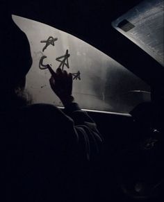 a person writing on the windshield of a car in the dark, with other cars behind them