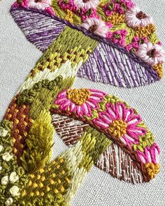 some very pretty colorful flowers on a white cloth with embroidery work in the middle and bottom