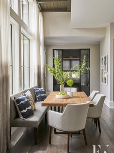 the dining room table is surrounded by white chairs and gray upholstered benches with blue pillows on them