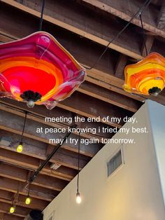 three colorful lights hanging from the ceiling in a building with a quote written on it