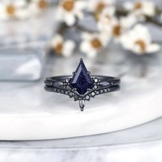 a black diamond ring sitting on top of a white marble slab with flowers in the background