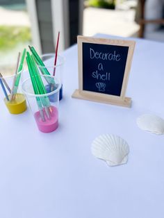 there is a chalkboard with writing on it next to plastic cups and seashells