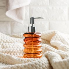 an orange soap dispenser sitting on top of a white blanket next to towels