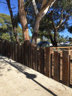 a car parked behind a wooden fence next to some trees and dirt road with cars in the background