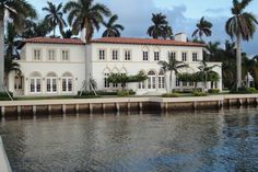 a large white house sitting next to a body of water with palm trees in front of it