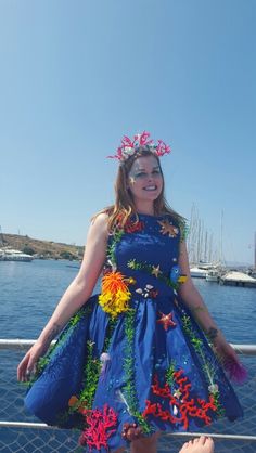 a woman in a blue dress with flowers on her head standing next to the water