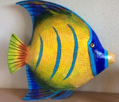 a blue and yellow fish sitting on top of a wooden table next to a white wall