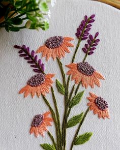 an embroidery project with orange and purple flowers on white fabric next to green stems in vase