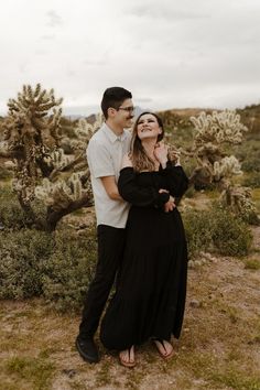 a man and woman standing next to each other in front of cacti