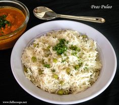 a white bowl filled with rice and vegetables next to a spoon on a black table