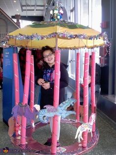 a woman standing in front of a pink and yellow carousel with dragon figures on it