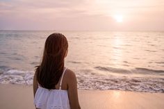 a woman standing on top of a sandy beach next to the ocean at sunset or dawn