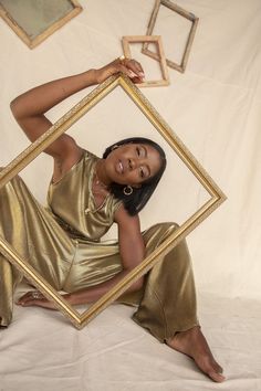 a woman sitting in front of a gold frame