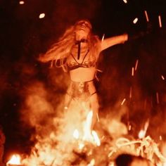 a woman standing on top of a fire with her arms outstretched in front of flames