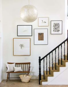 a staircase with pictures hanging on the wall and a bench in front of it under a light fixture