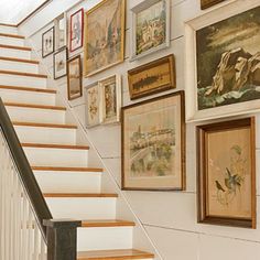 there are many framed pictures on the wall next to the stair case in this house