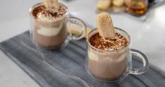 two mugs with hot chocolate and whipped cream in them on a gray place mat