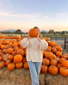 a woman standing in front of a pile of pumpkins with her hands on her head