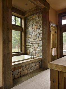 a bathroom with stone walls and flooring next to a bathtub in front of a window