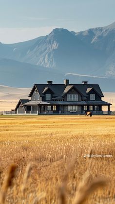 a large house sitting in the middle of a wheat field with mountains in the background