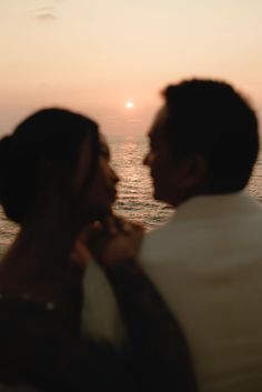 a couple standing next to each other in front of the ocean at sunset or sunrise