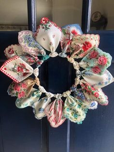 a wreath made out of cloths hanging on the front door with flowers and ribbons around it