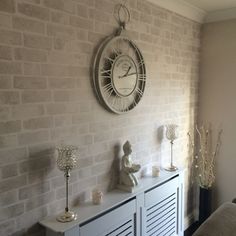 a clock mounted to the side of a brick wall next to a white cabinet with drawers