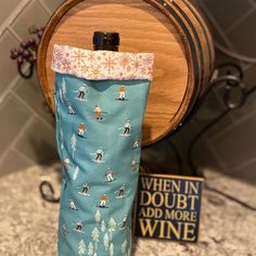 a wine bottle bag with skiers on it sitting on a counter next to a wooden barrel